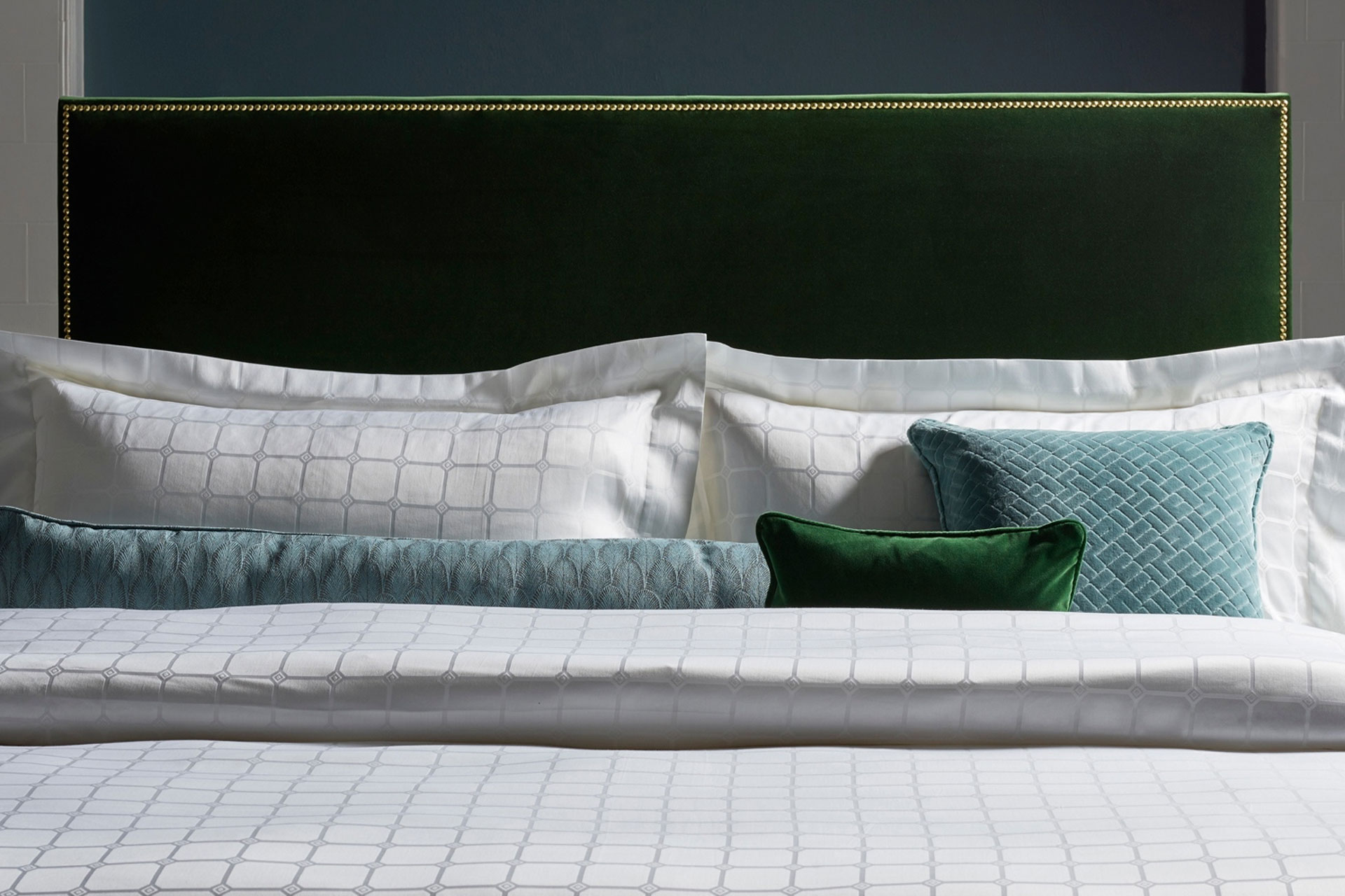 a front view of a luxury bed with pillows and cushions on a green velvet headboard by Savoir Beds
