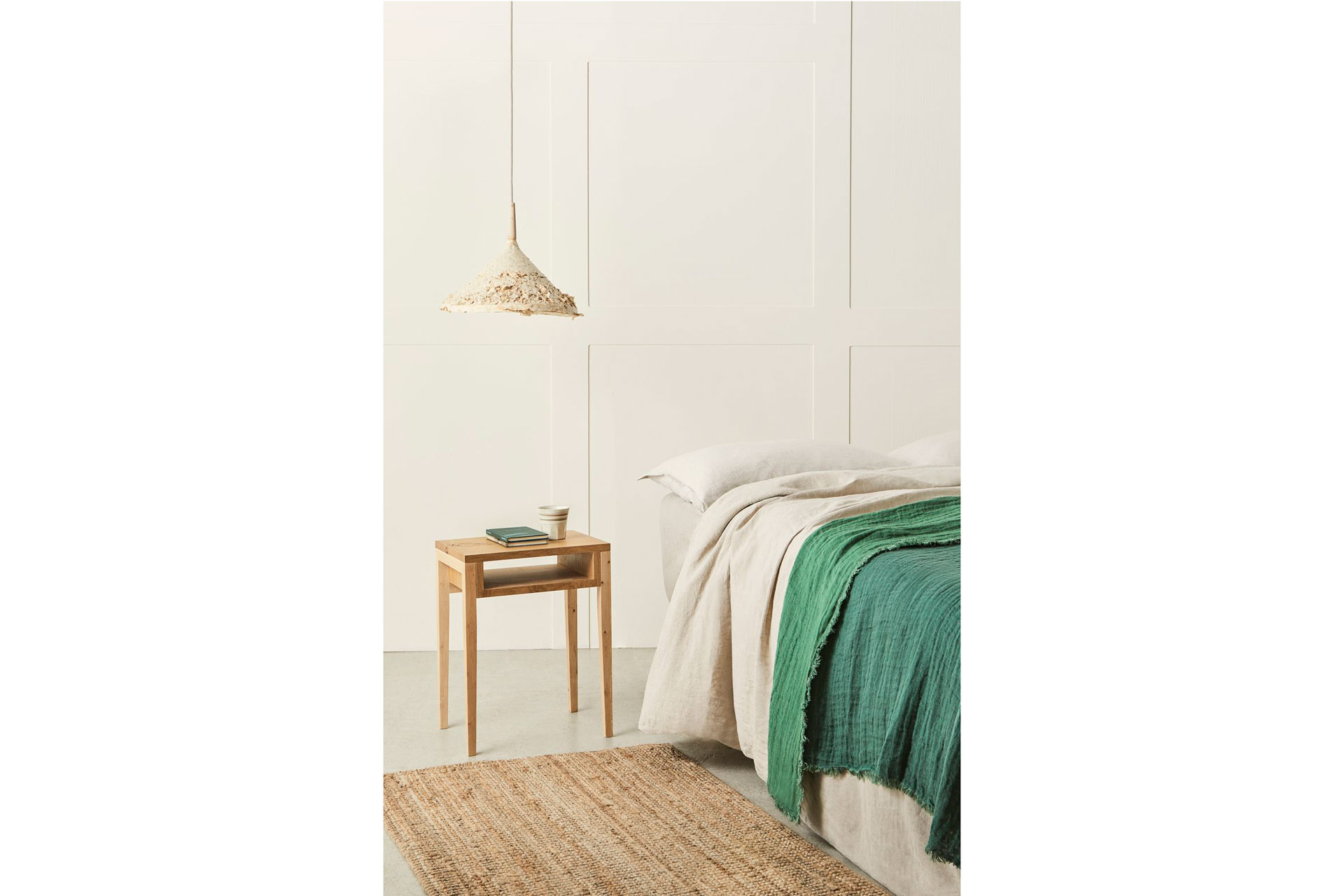 a wooden side table and a bed with green linen by Sebastian Cox, a furniture maker