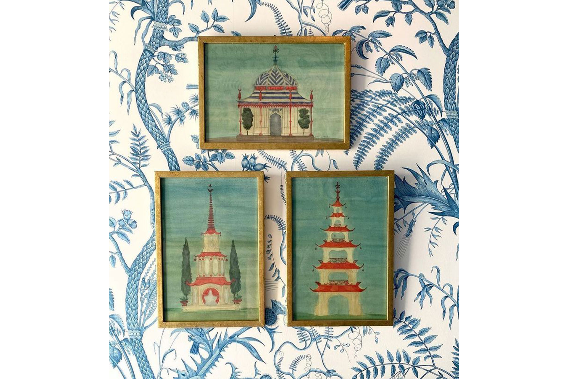 three 'folly' paintings on a background of blue floral wallpaper