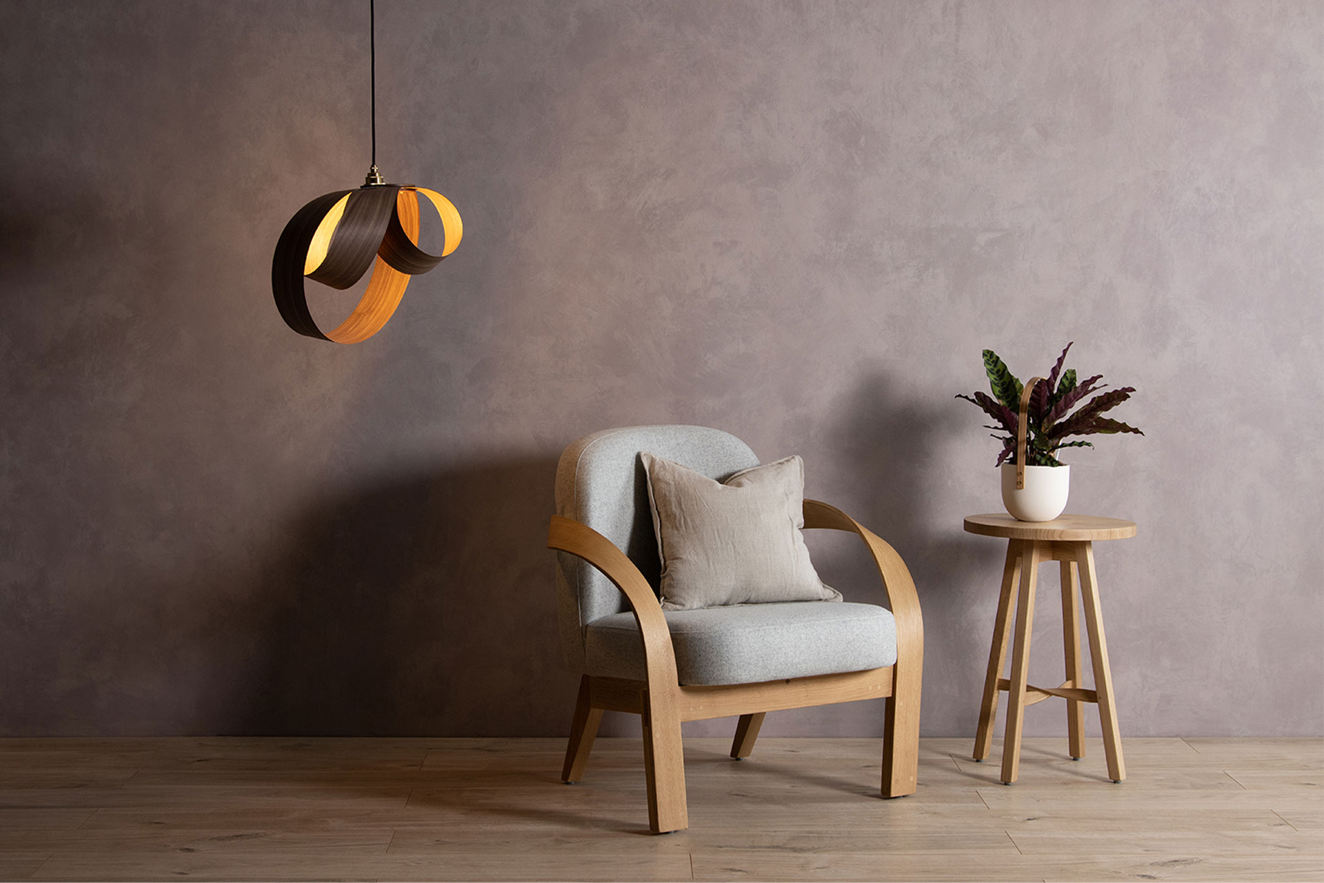 a minimalist living room with a cream armchair, wooden stool, and ceiling light made from wood strips, that's designed by Tom Raffield