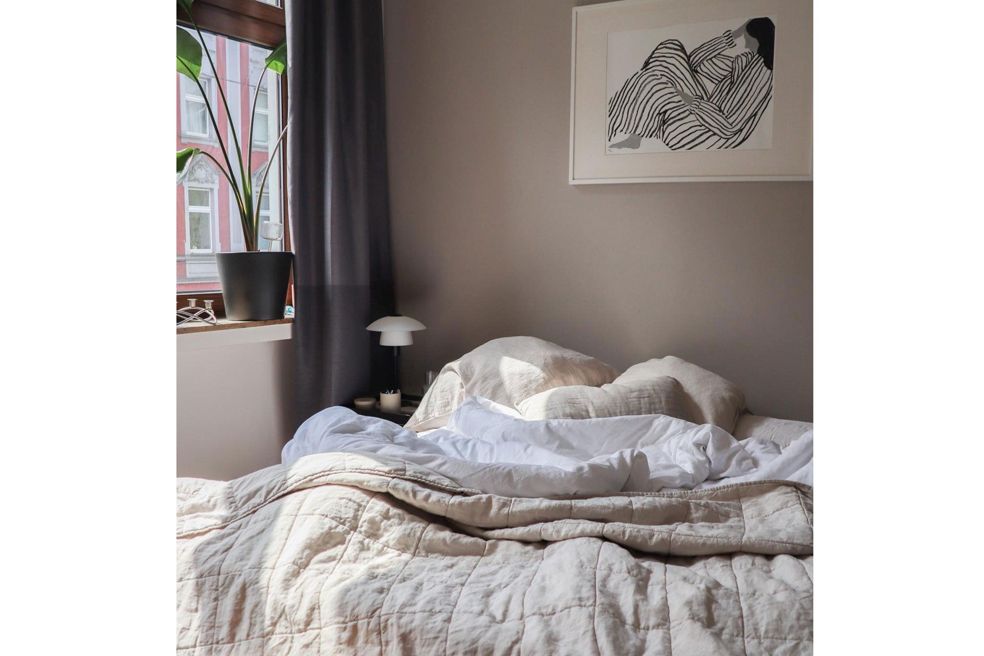 a bedroom with a grey wall and cosy bed with a cream quilted blanket with a window on the left by Urbanara