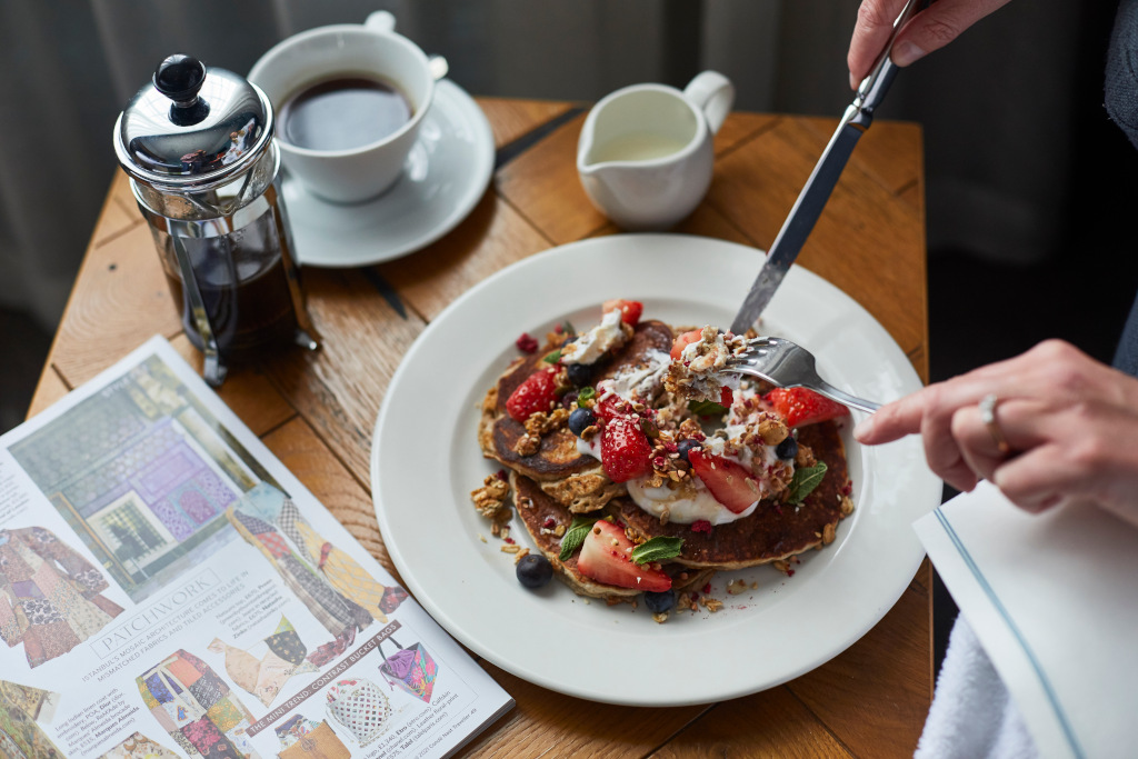 knife and fork tucking into stack of pancakes with strawberries