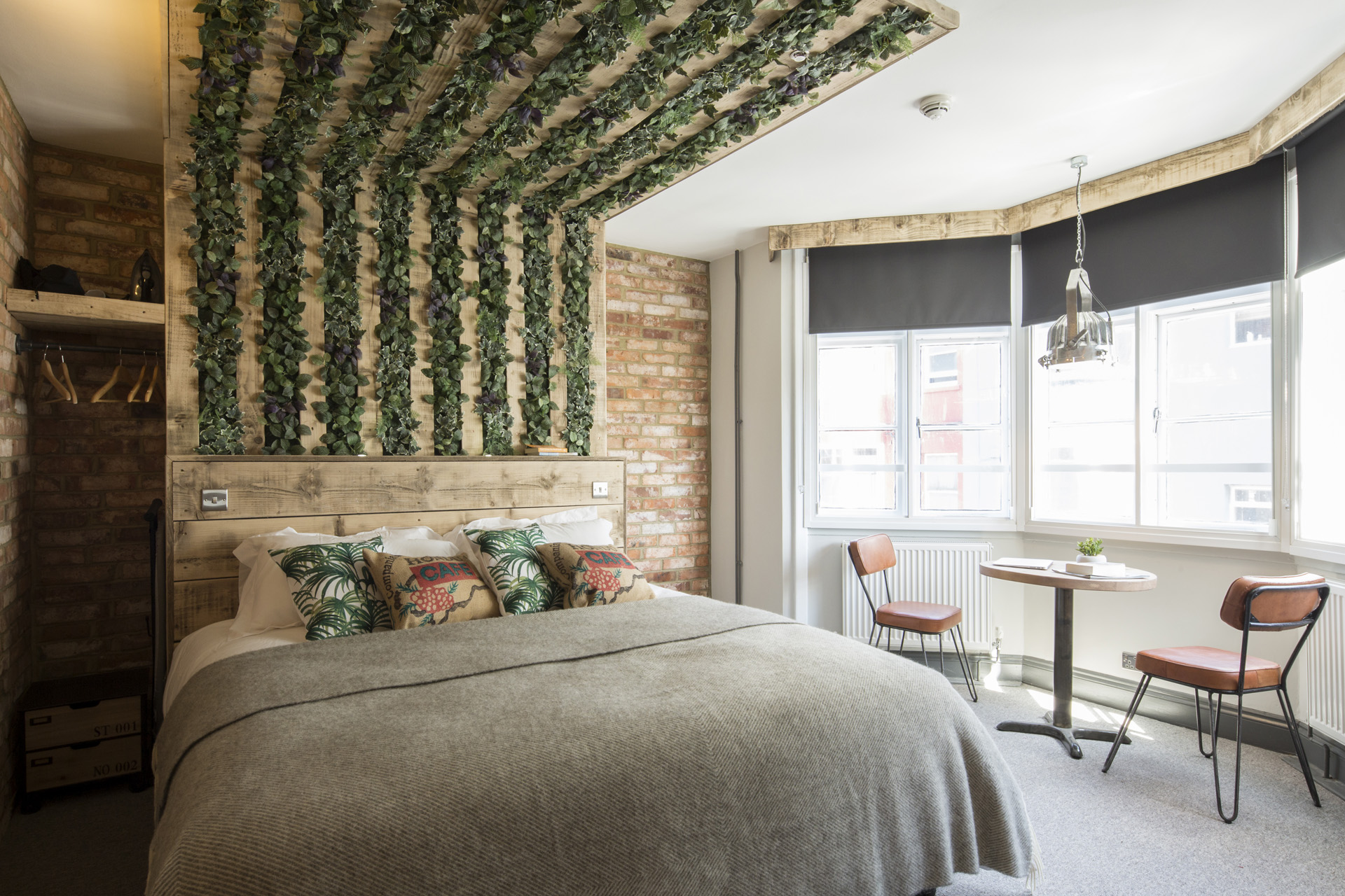 a double bed with foliage design and bay window with table and chairs
