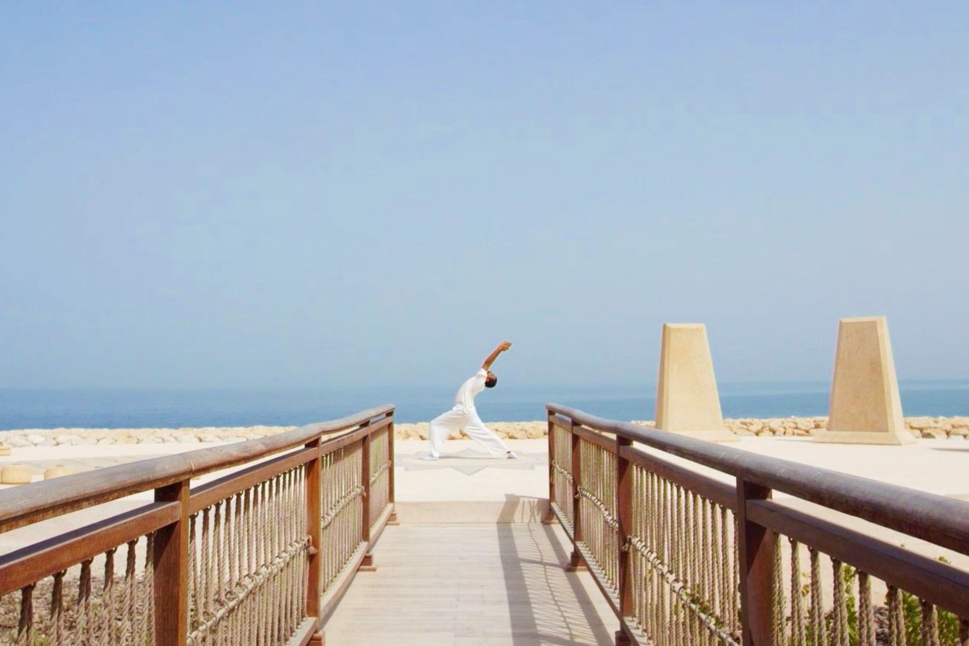 shot of bridge walkway going to beach on banana island qatar with someone doing yoga