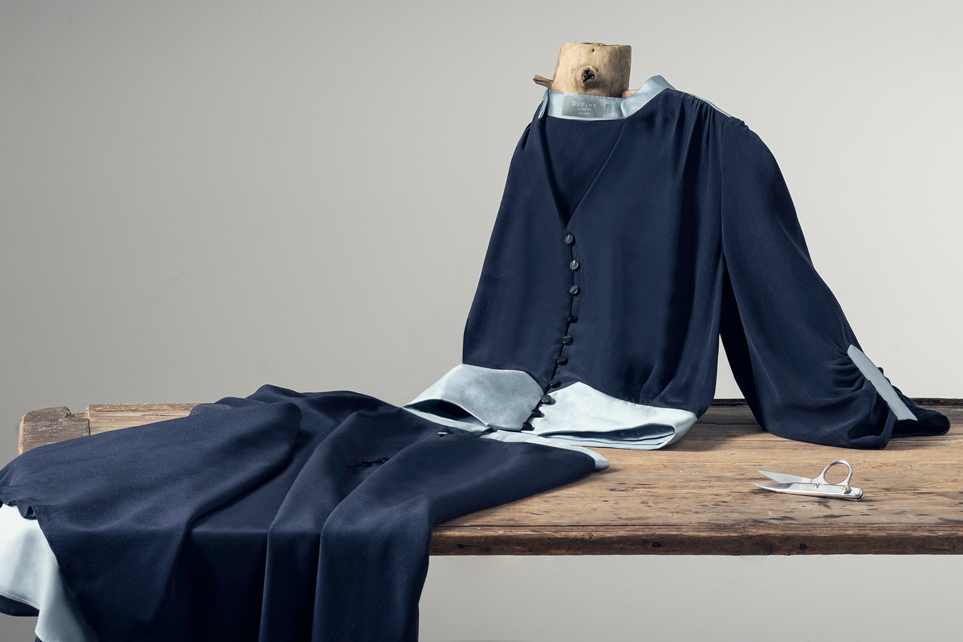 Navy clothing items draped over a wooden table, with a neutral background