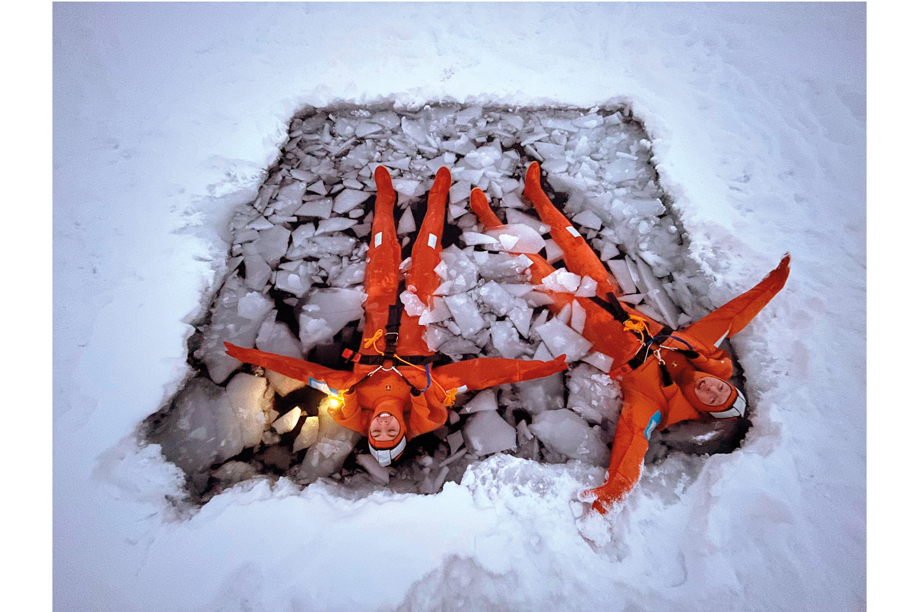 Two people in orange suits floating in a pool of ice