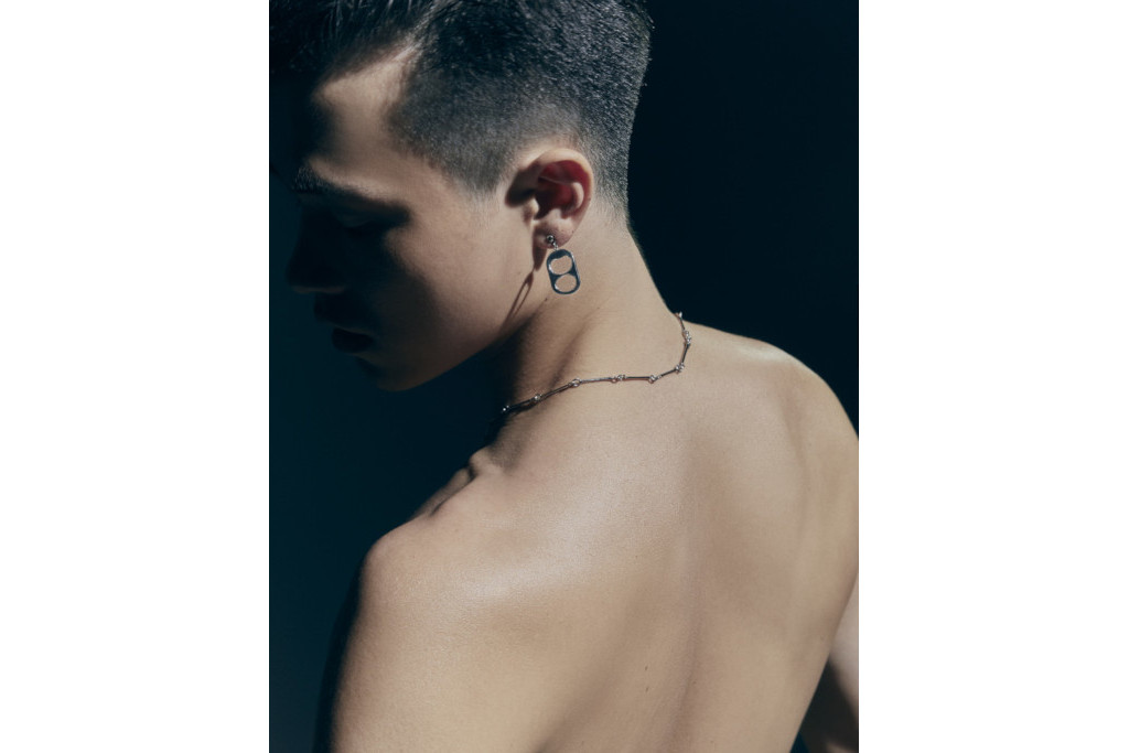 Model is deep shadow looking over his shoulder, wearing a necklace and earring