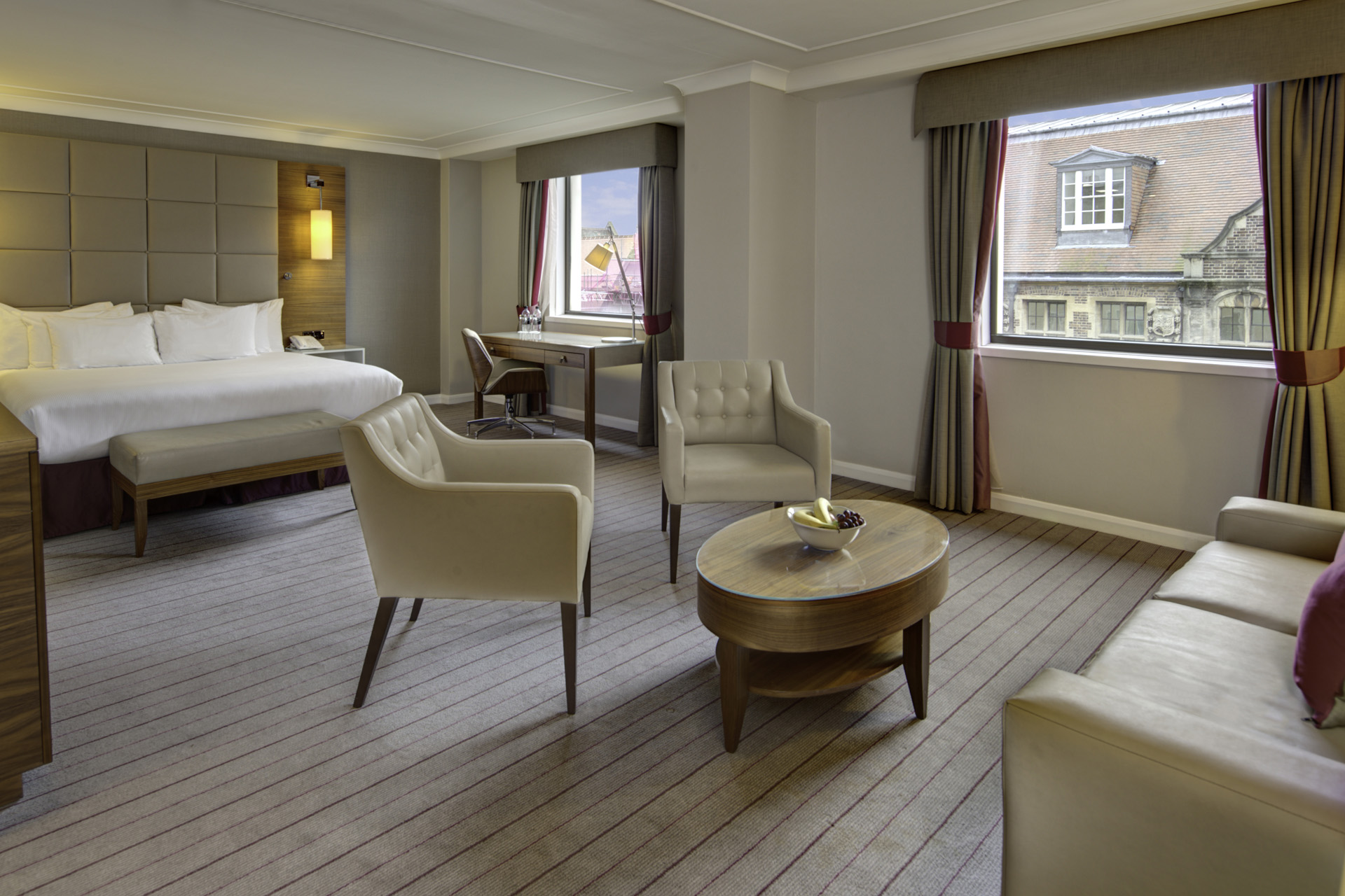 A spacious hotel room with bed, two windows and sitting area
