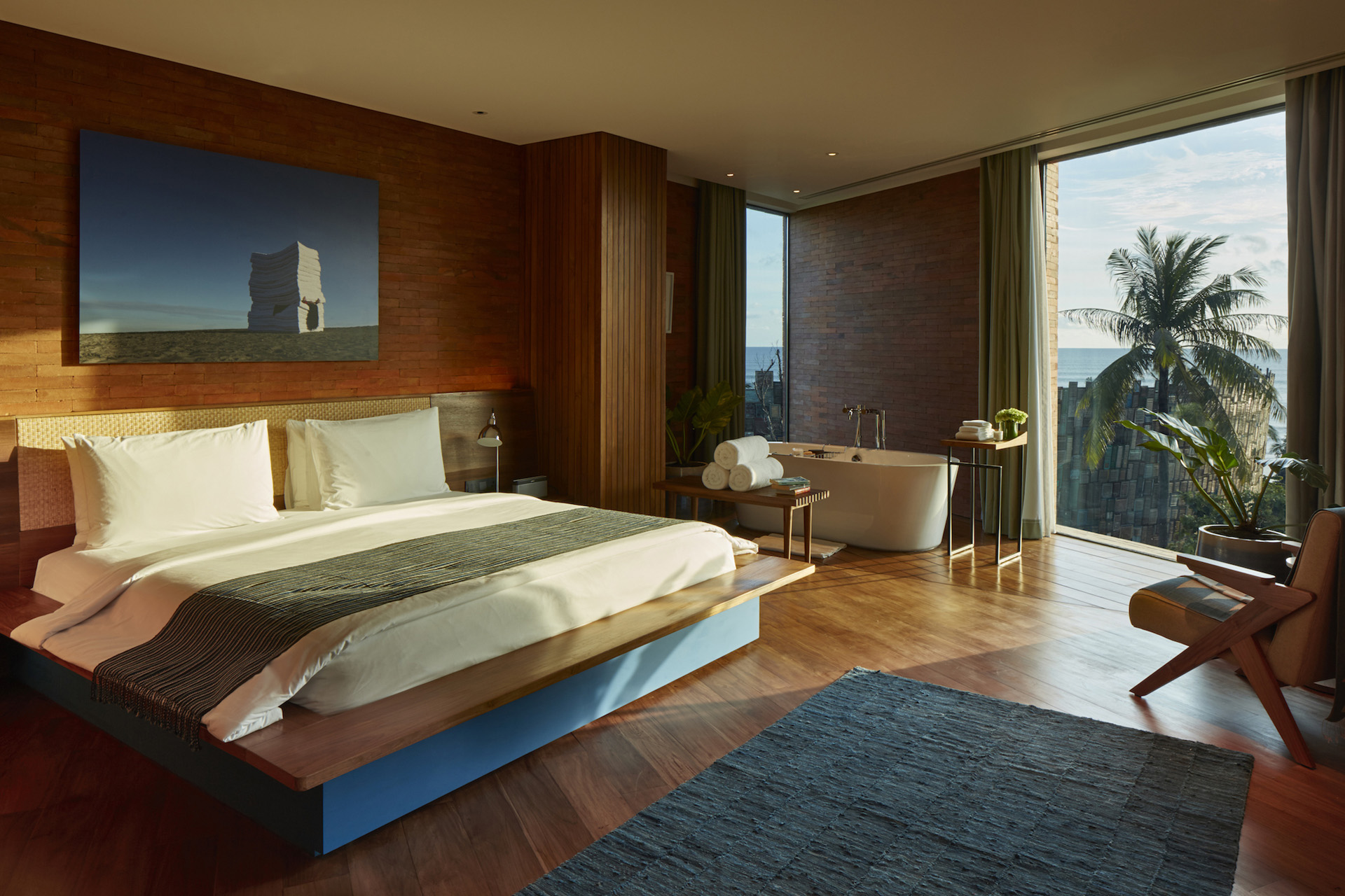 A bed in an open plan room with bathtub at golden hour