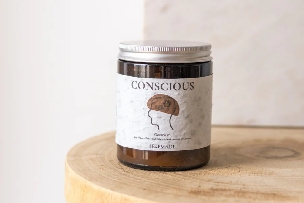 Candles jar with 'conscious' label, set on wooden surface