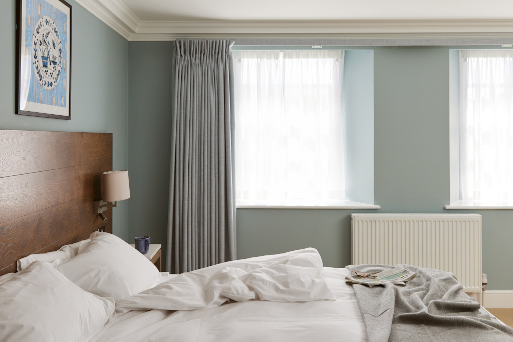 side view of bedroom with blue walls and cosy bed with newspaper and duvet untucked