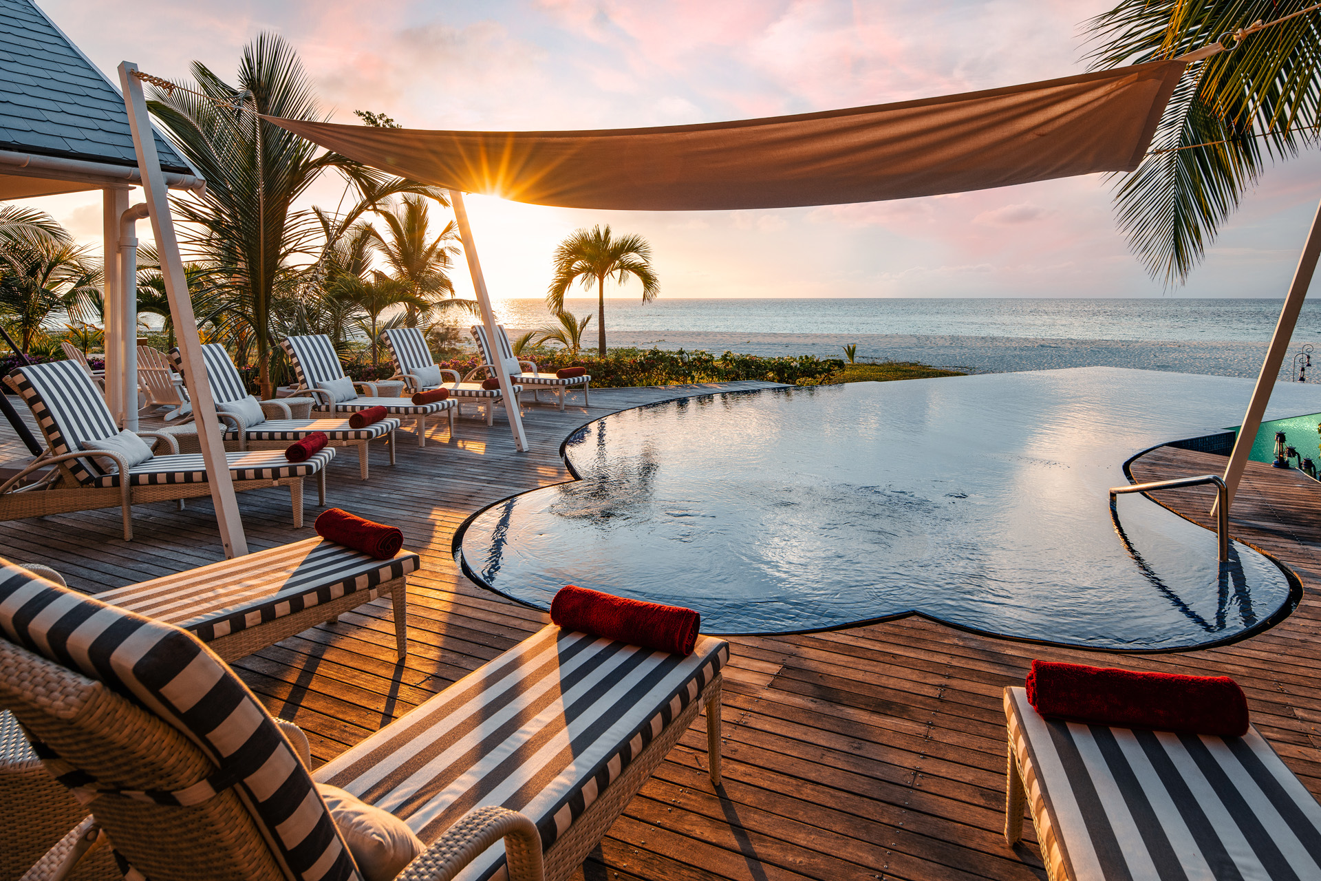 An infinity pool at dusk surrounded by striped deck chairs and palm trees