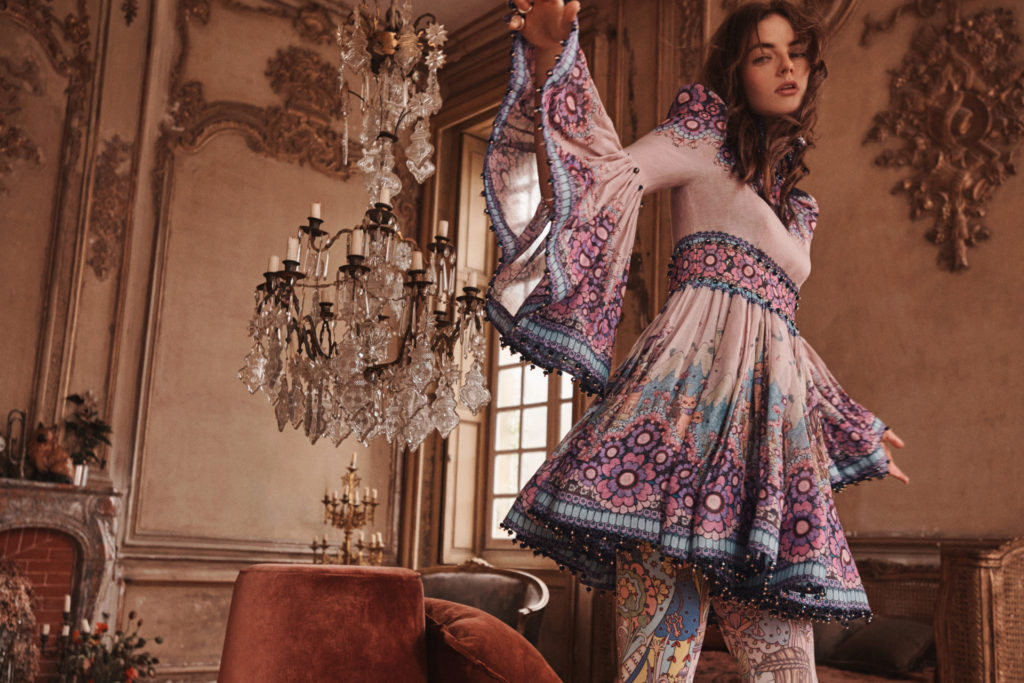 Model in ornate living room wearing a bell-sleeved mini dress, with a chandelier in the background