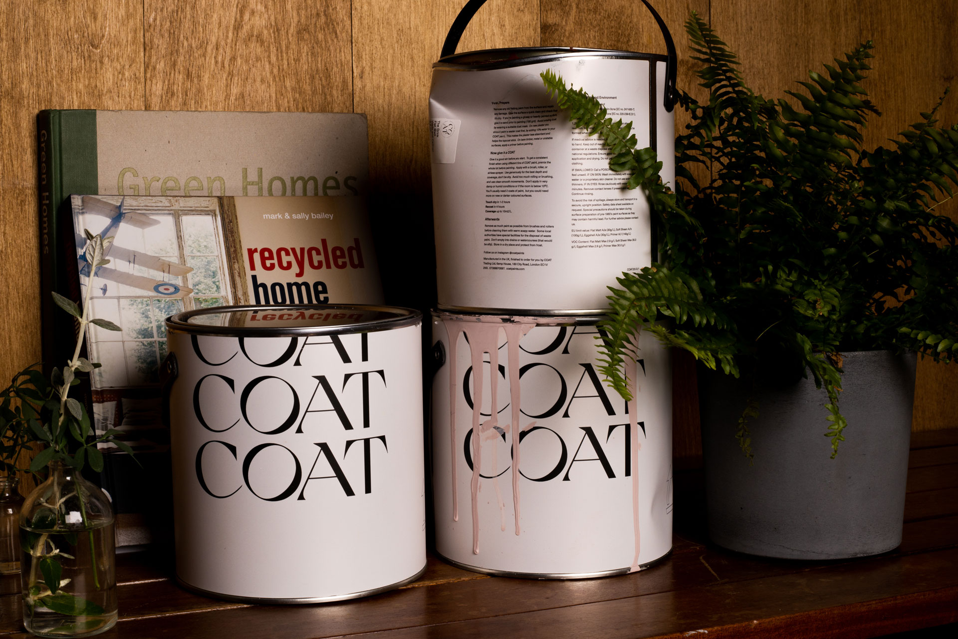 a stack of coat paints on a shelf with a plant. Coat is the first B Corp Paint Brand