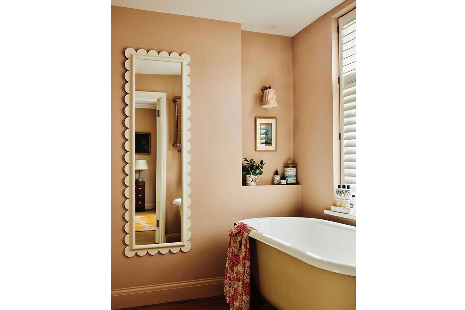 a pink bathroom with a yellow bathtub and scalloped mirror
