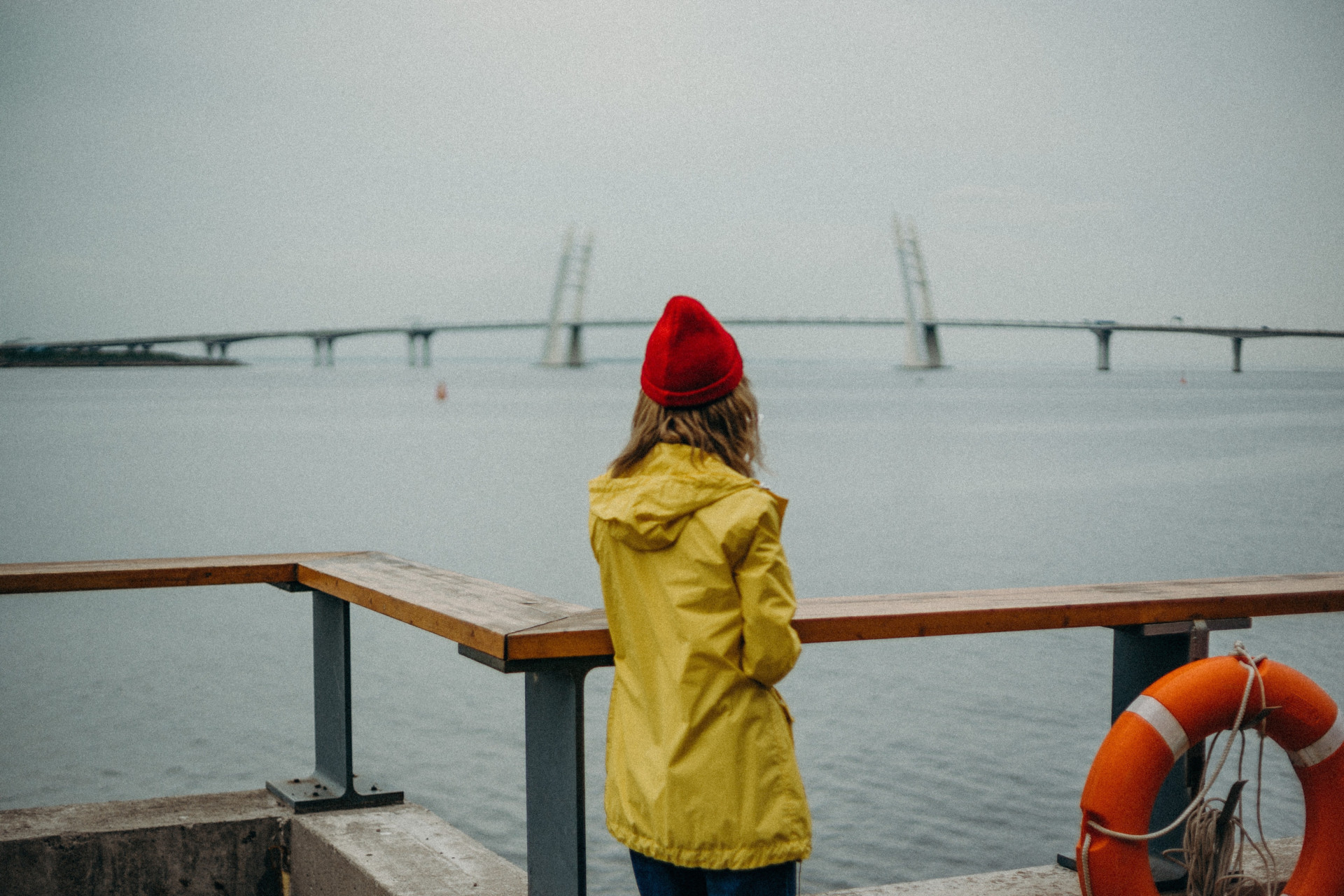 Woman in yellow raincoat and red hat looking out to sea