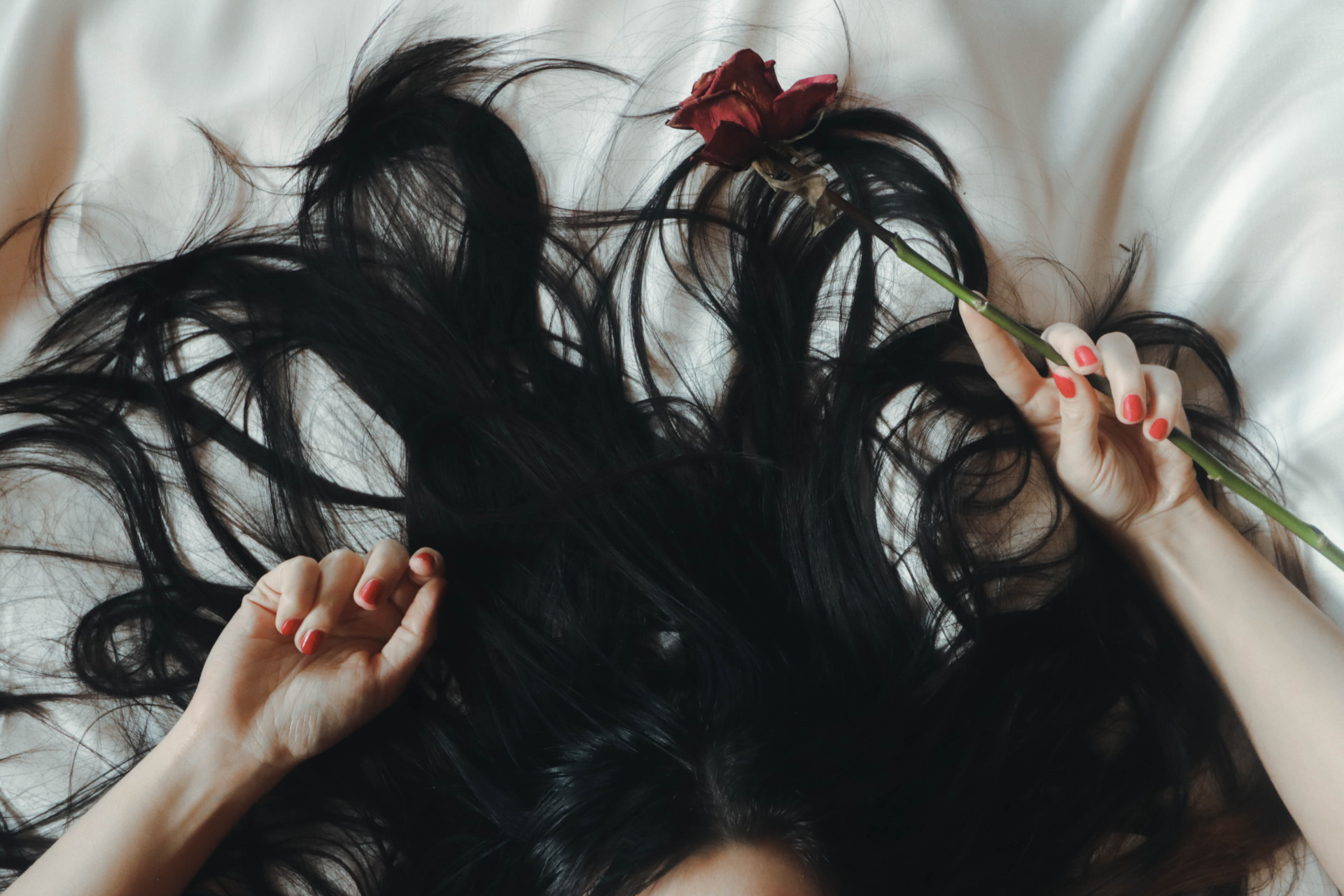 Close up of woman's hair as she lies on a bed with arms up and a rose in her hand