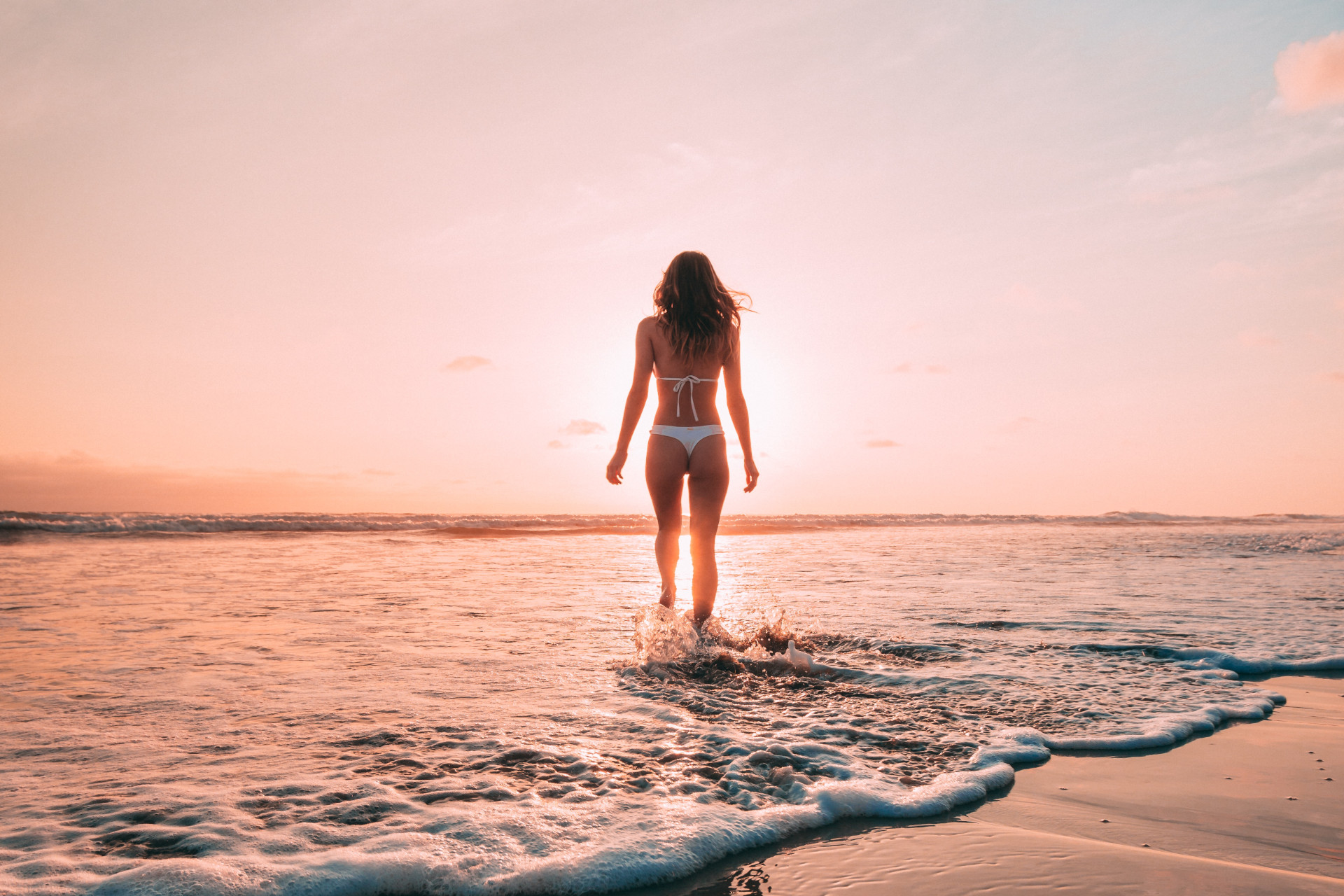 Woman on a beach at sunset facing the ocean