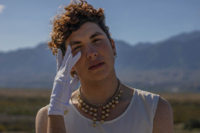 Man wearing pearls necklaces and white gloves stood outdoors in the sun
