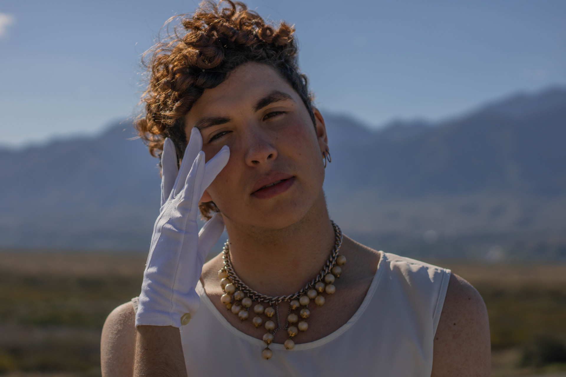 Man wearing pearls necklaces and white gloves stood outdoors in the sun