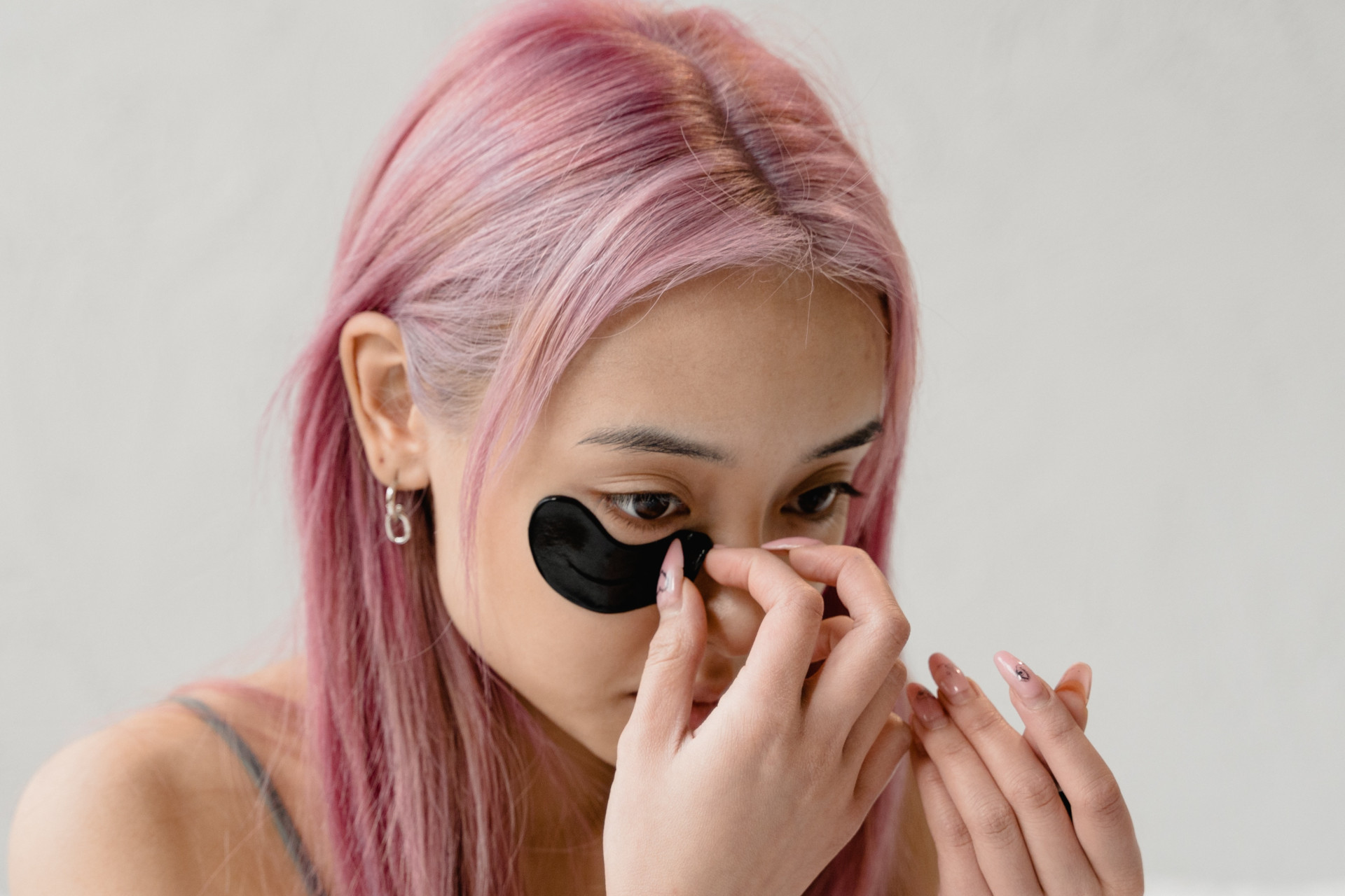 Woman with pink hair applying black eye mask