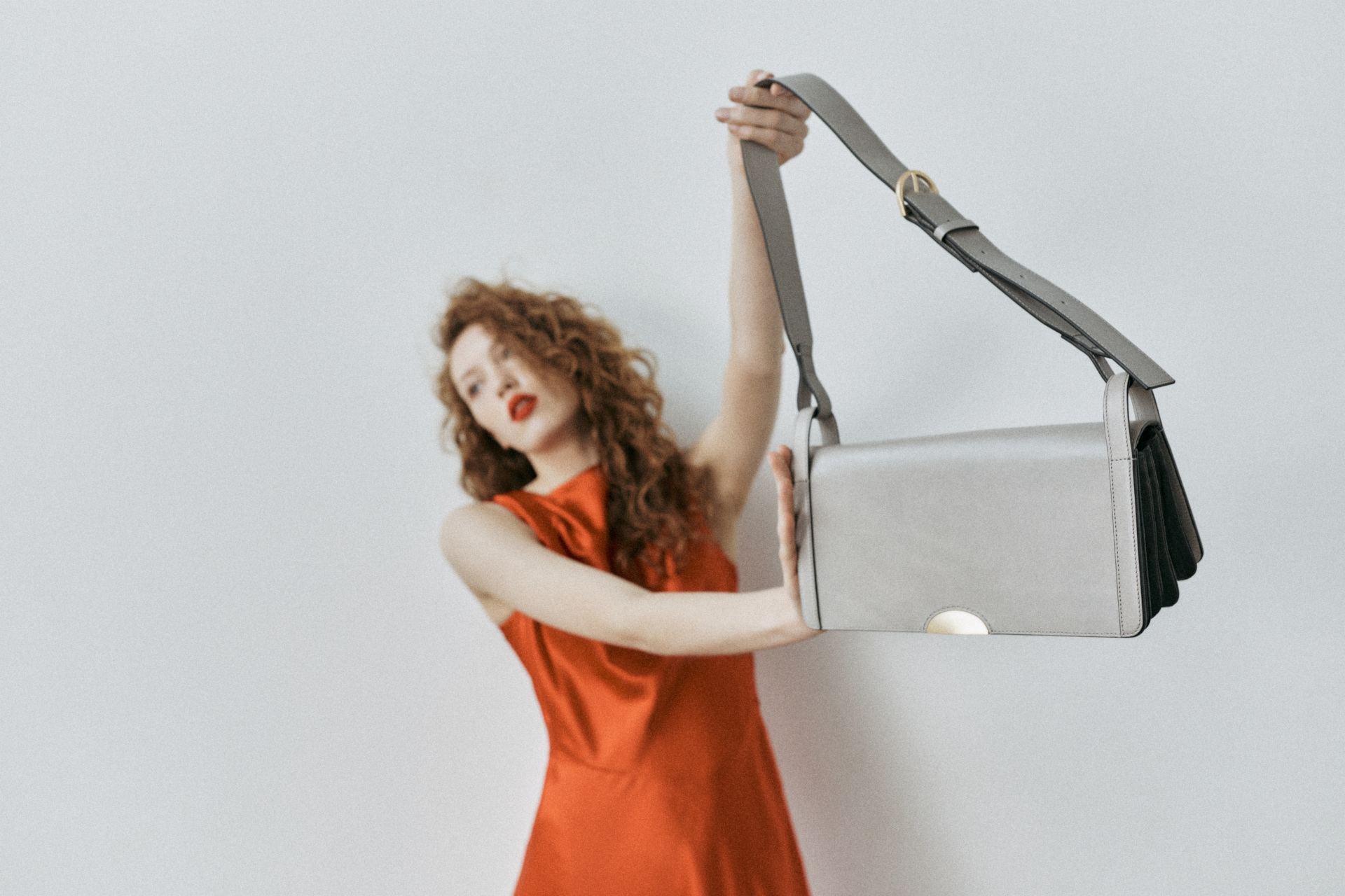 Woman in orange dress holding bag up to the camera so that she's out of focus