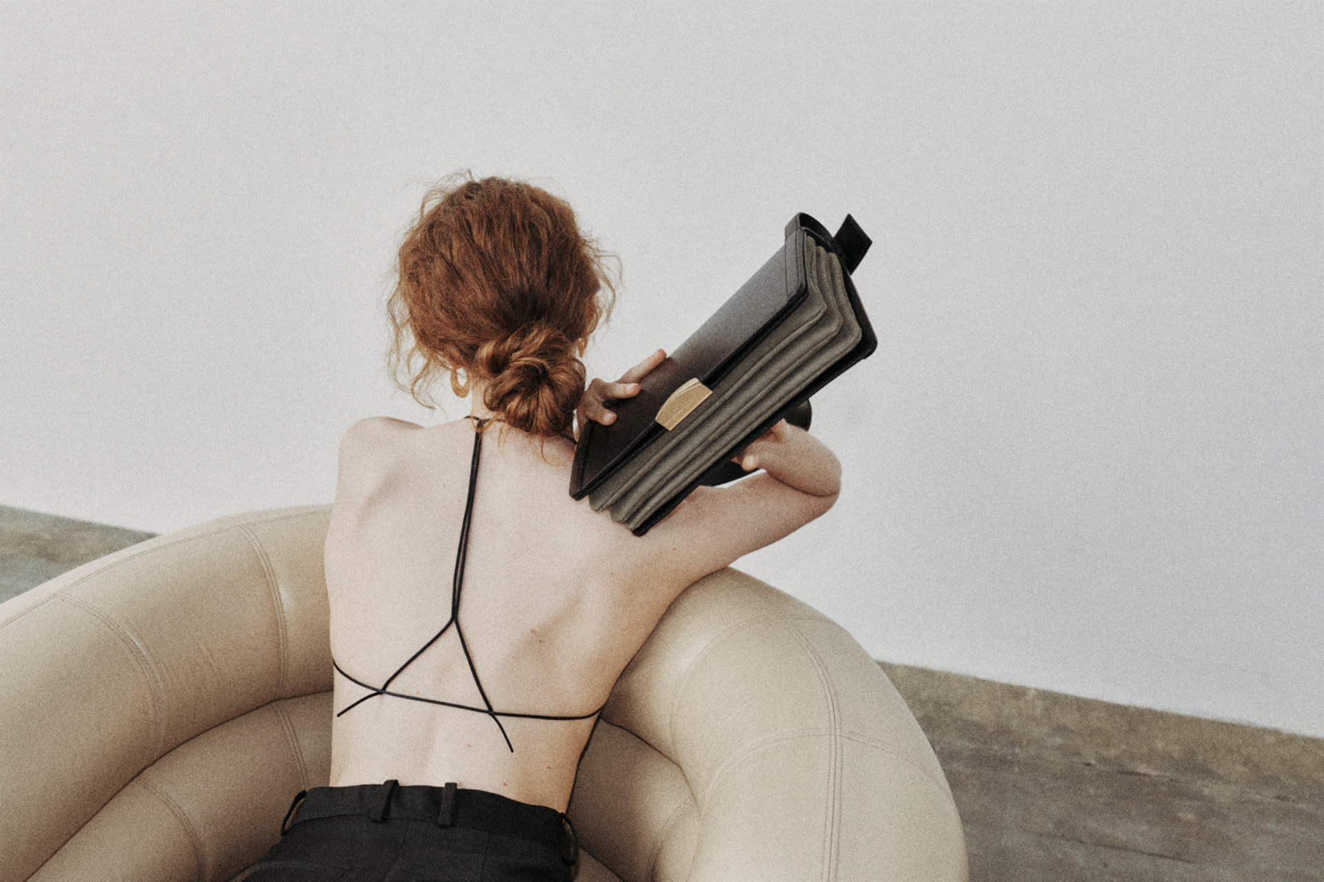 Woman leaning over the back of an armchair with her back to the camera, a clutchbag in her hand slighlty over her shoulder