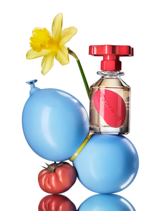 Large glass bottle with red screw top resting on a blue balloon next to dandilion