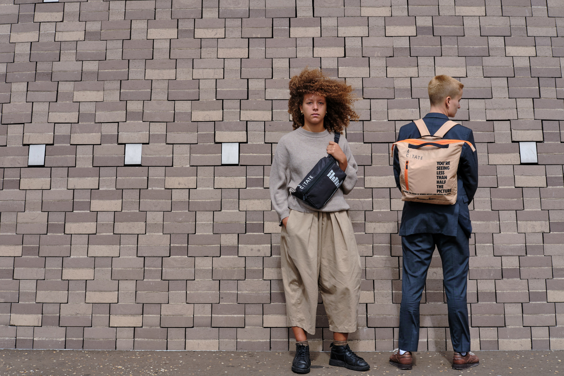 Models stood in front of brick wall wearing street clothes and bags