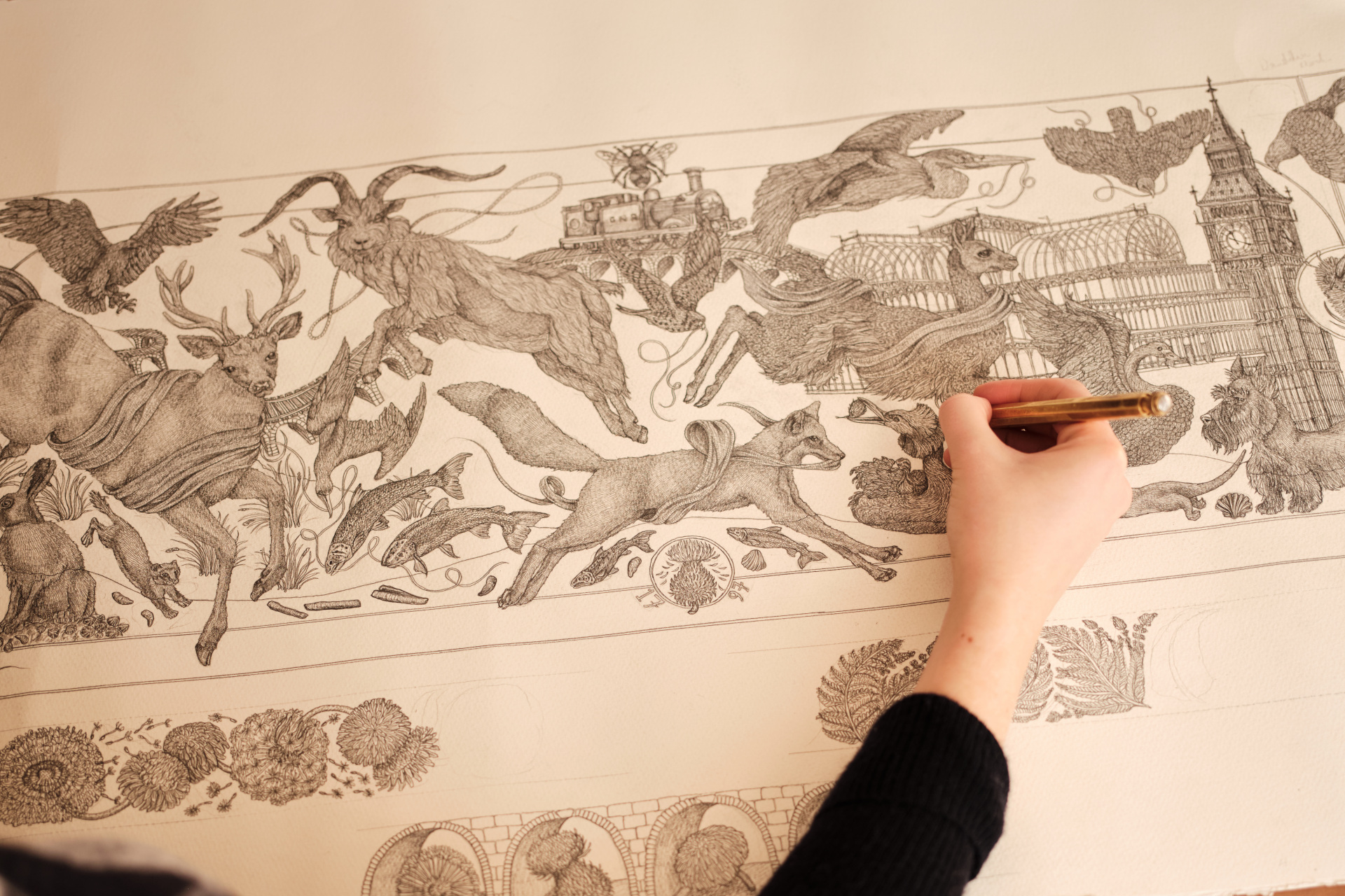 Close up of hand drawing out an intricate design of animals and London landmarks