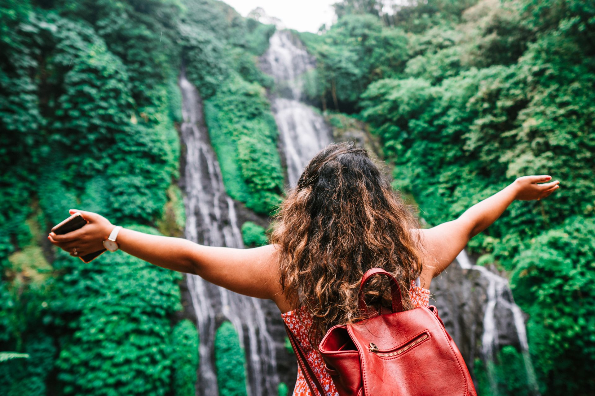 Woman with long air and backpack in front of a waterfall