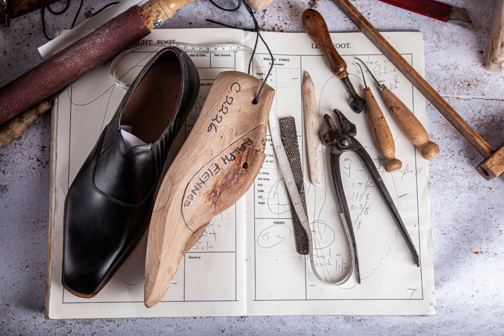 Shoes and measuring tools set out on notebook on workbench - British shoe brands