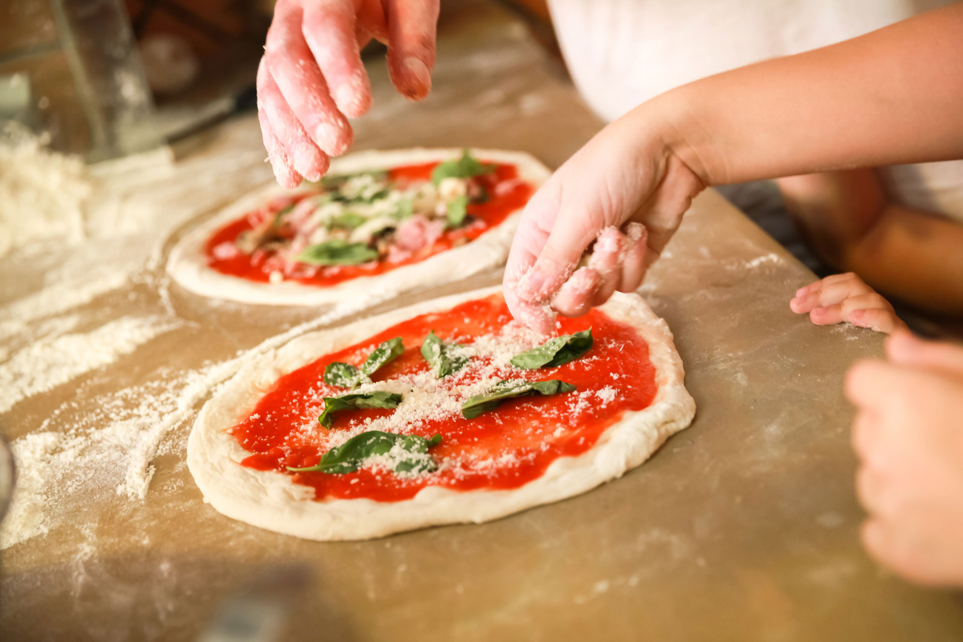 Two pizzas with basil leafs scattered on top of tomato sauce