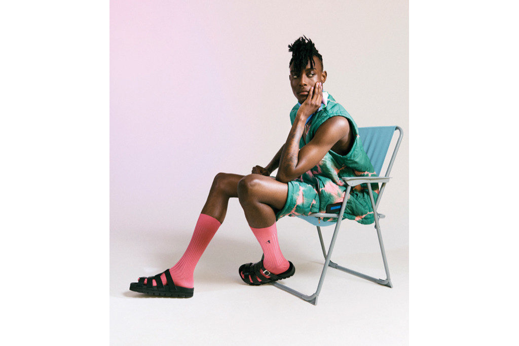 Model leaning back on blue deck chair while wearing pink socks and black slides