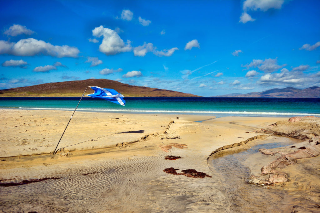 a beach with blue green waters and a scottish flag