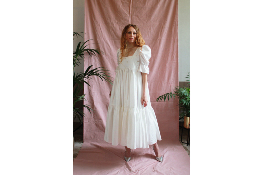 Model in oversized white dress stood in front of pink sheet