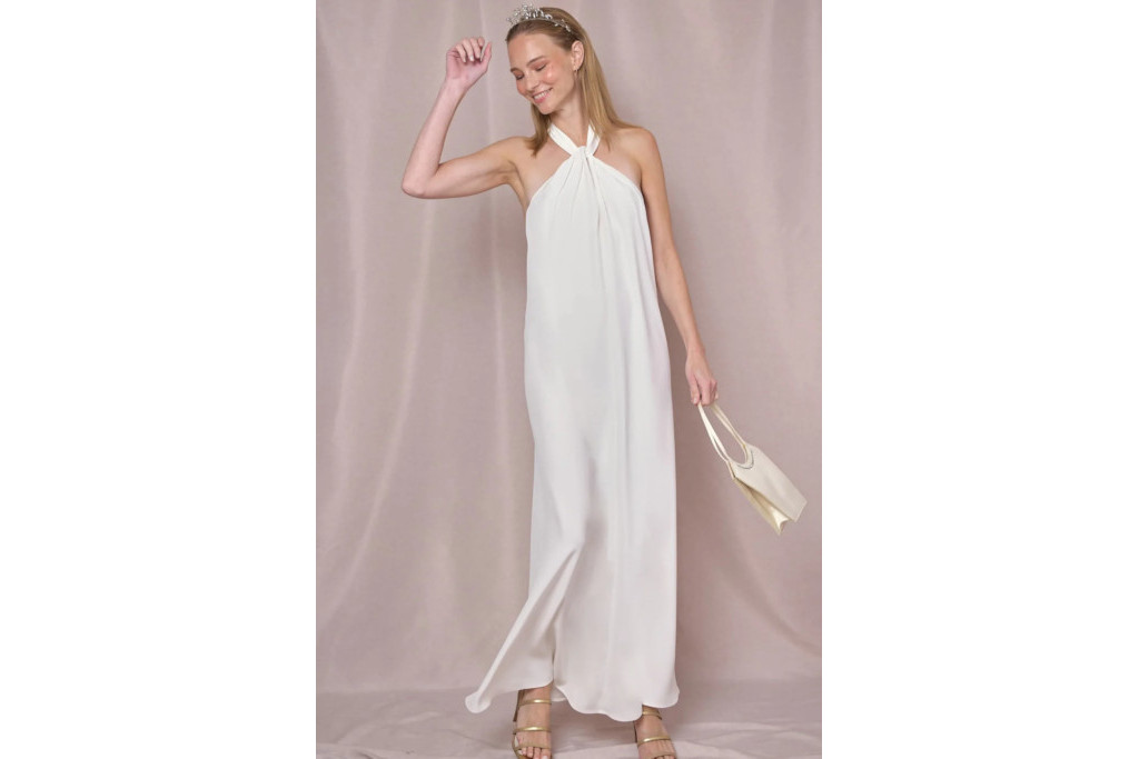 Model in white dress stood in front of light purple curtain