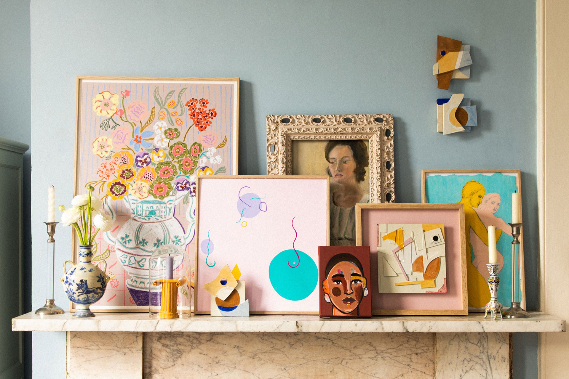 an assortment of framed paintings and prints on a fireplace shelf