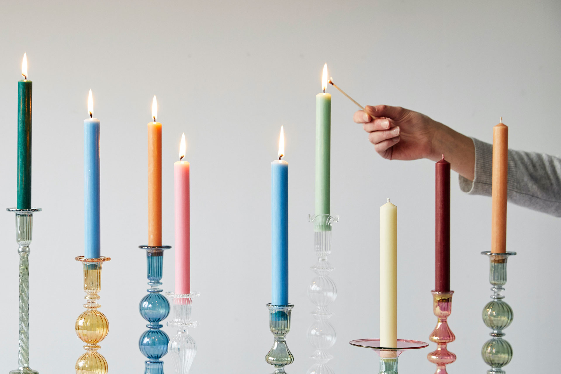 close up of a hand lighting an array of long colourful dinner candles with a match