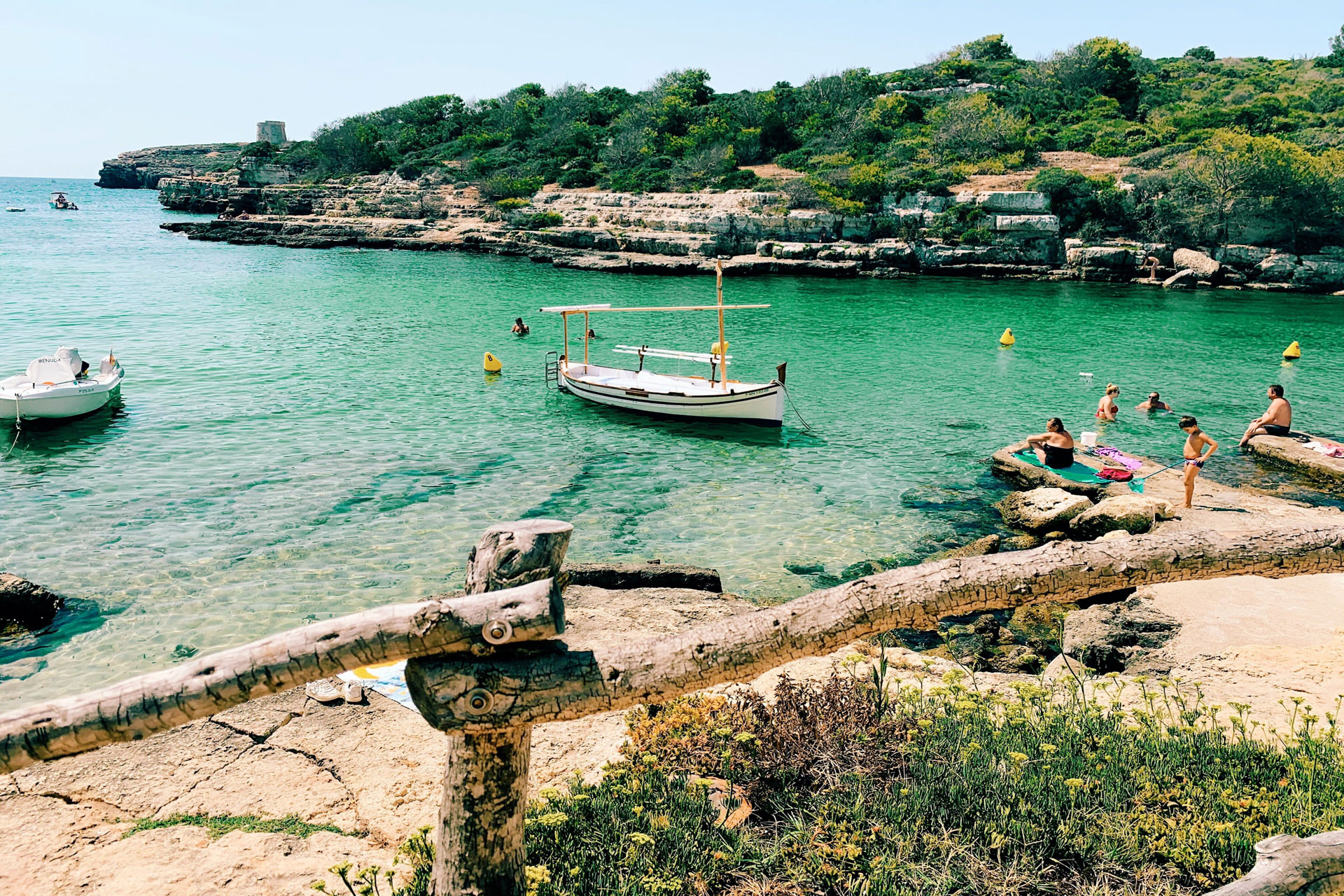 Turquoise ocean with tiny boat in the center and people relaxing on the shore