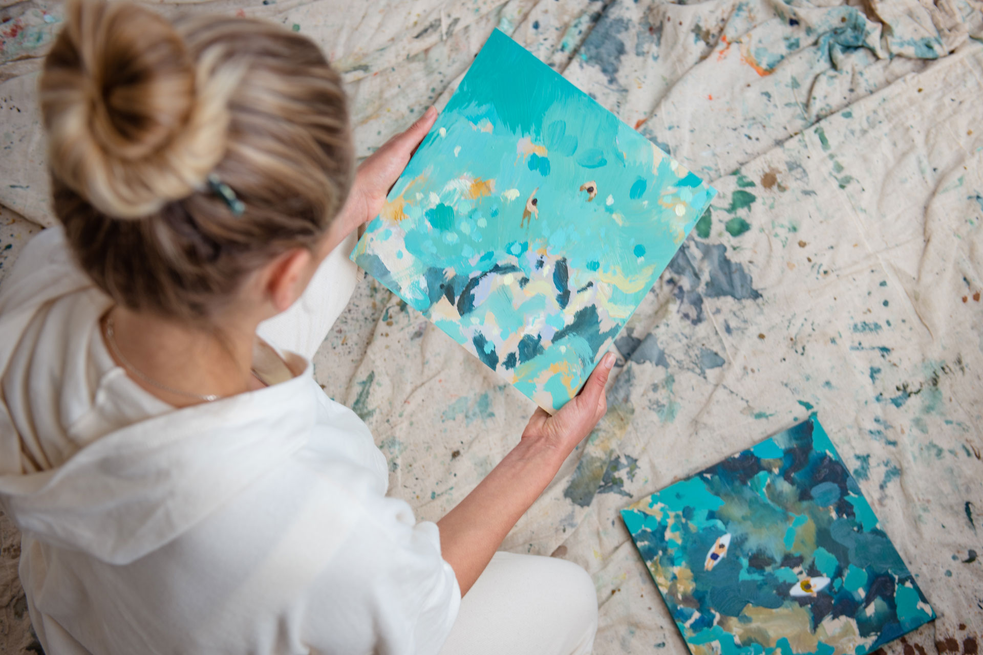 coastal artist Nina Brooke holds one of her seascape paintings in an artists studio