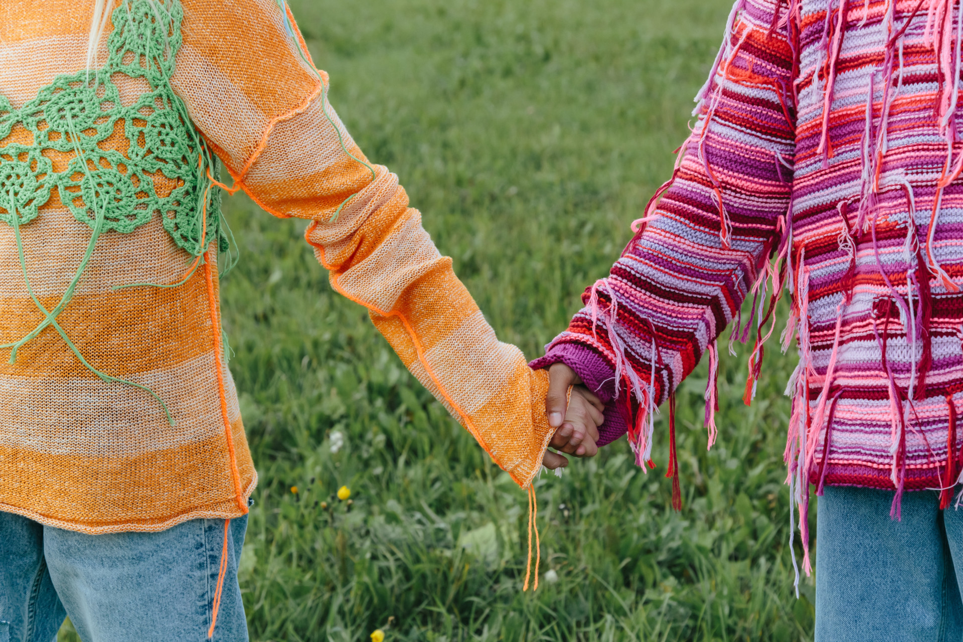 Two people holding hands in a field while wearing crochet jumpers