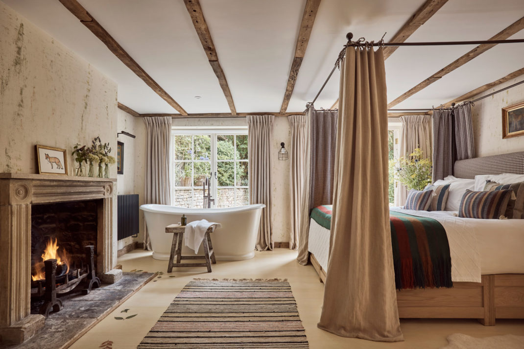 a canopy bed with wooden beamed ceilings and a fireplace and a freestanding bath tub feature at The Den suite at The Fox at Oddington
