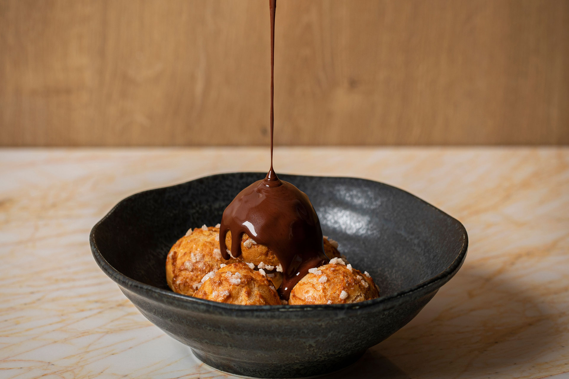 Black bowl filled with fried sweett treats with chocolate sauce drizzled over the top