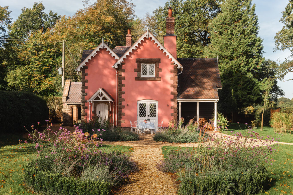 Charlotte's Folly in Shropshire, a cute pink cottage surrounded by grass with trees behind it