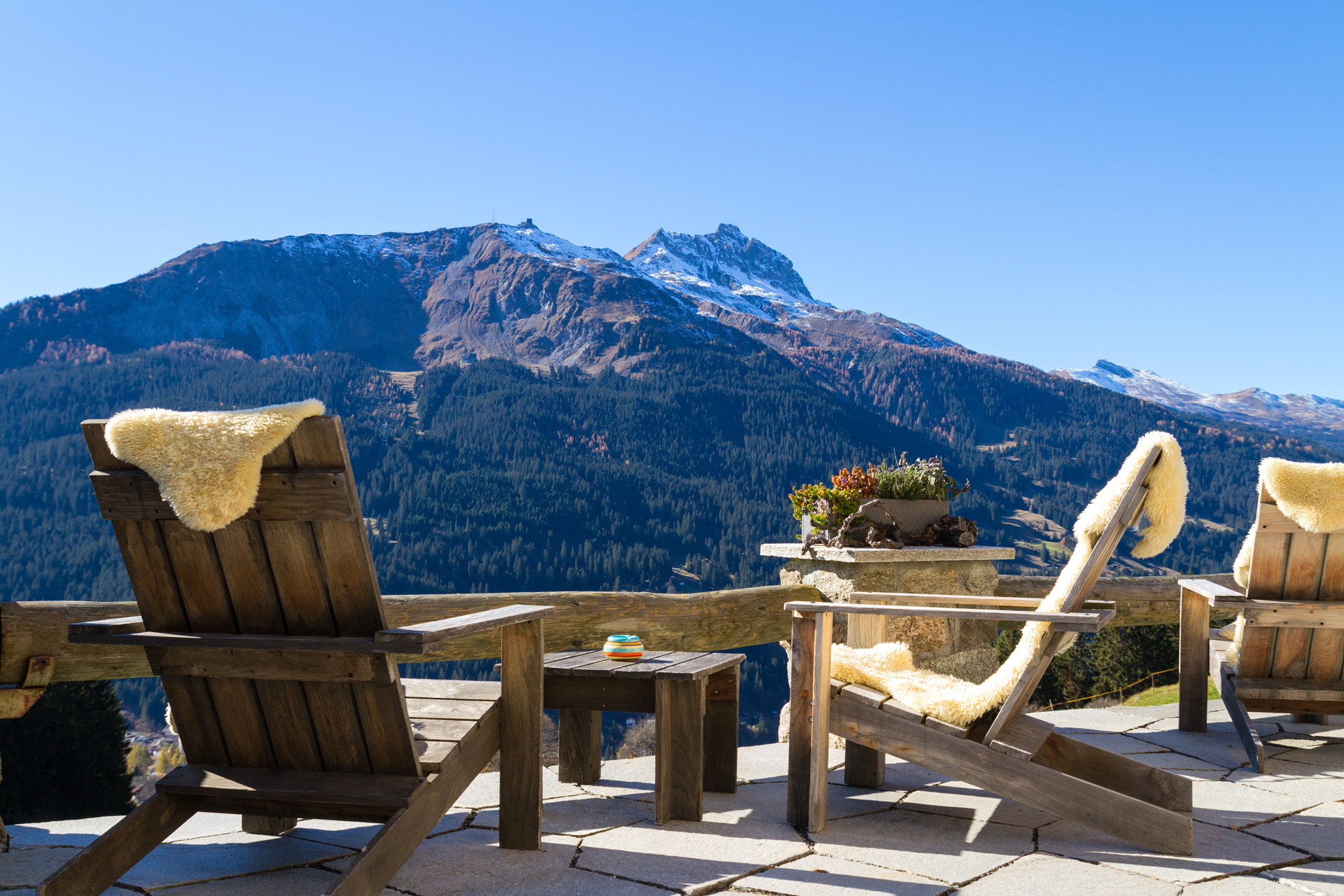 Wooden easy chairs at a mountain lodge terrace with panoramic view of beautiful alpine landscape in autumn at the Klosters - Davos region, Switzerland.