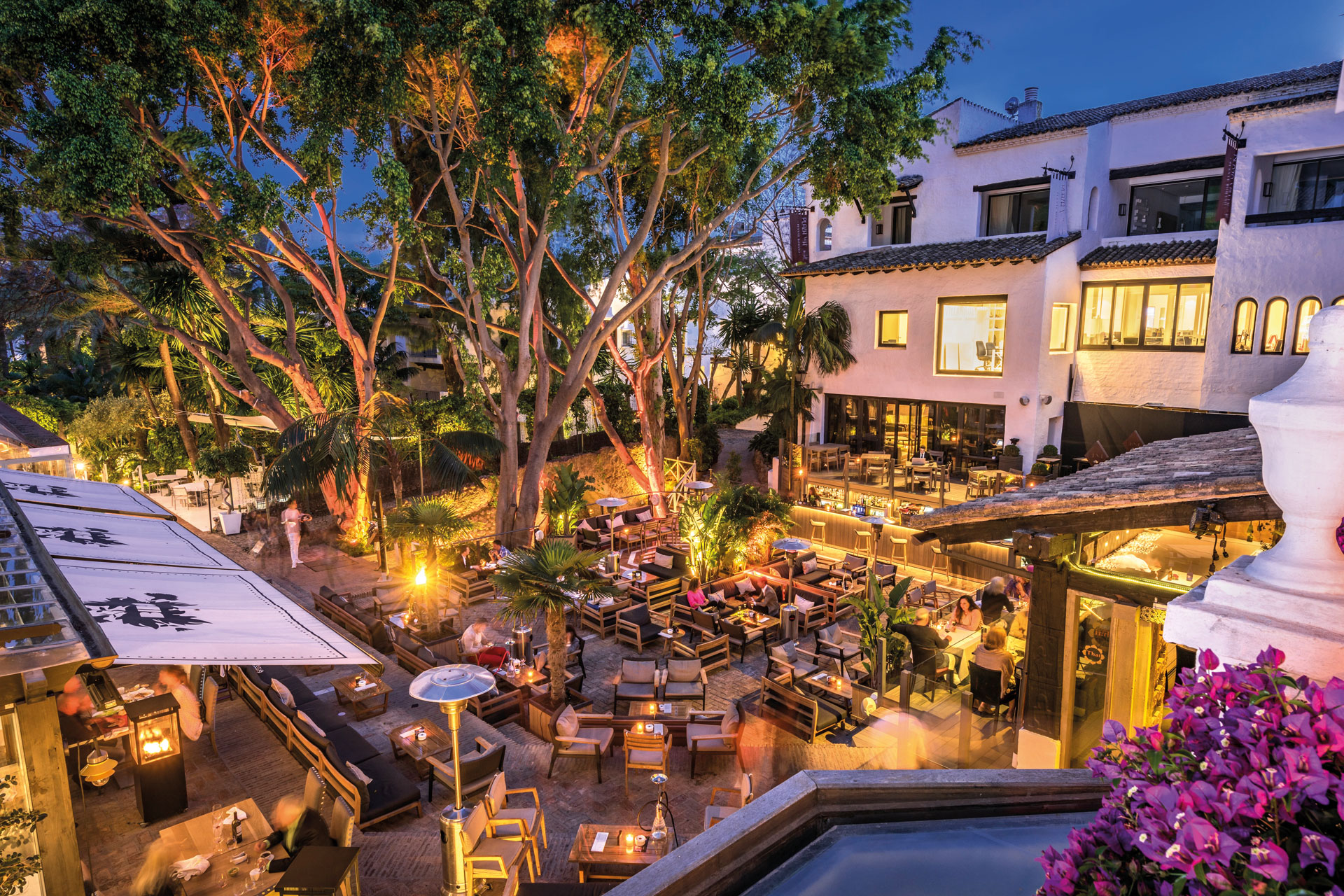 Plaza at night with dining tables and chairs dotted around 