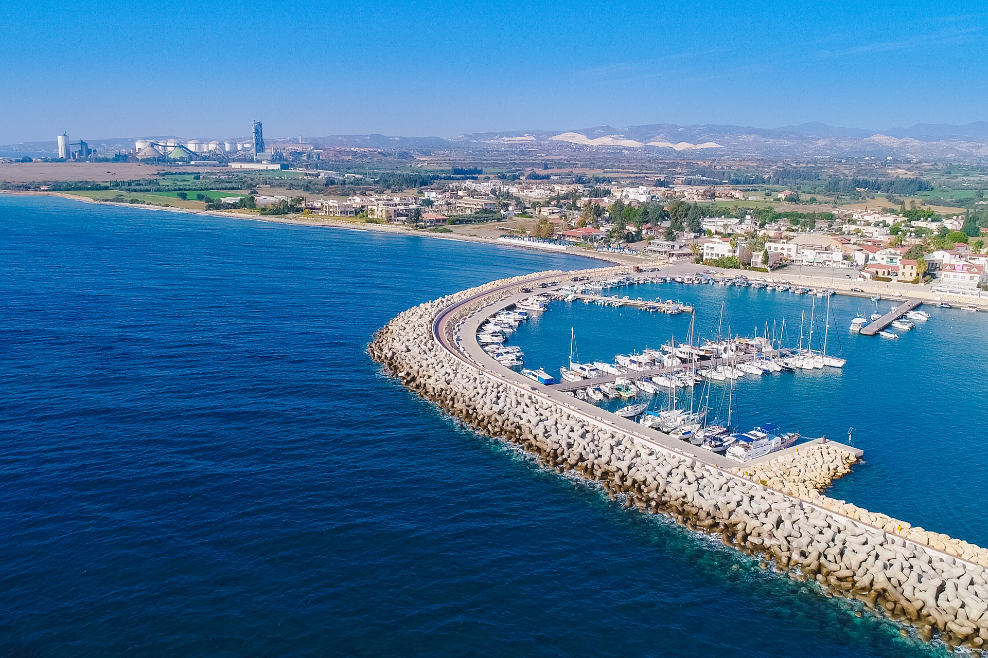 Aerial bird's eye view of Zygi fishing village port, Larnaca, Cyprus. The fish boats moored in the harbour with docked yachts and skyline of the town near Limassol from above.