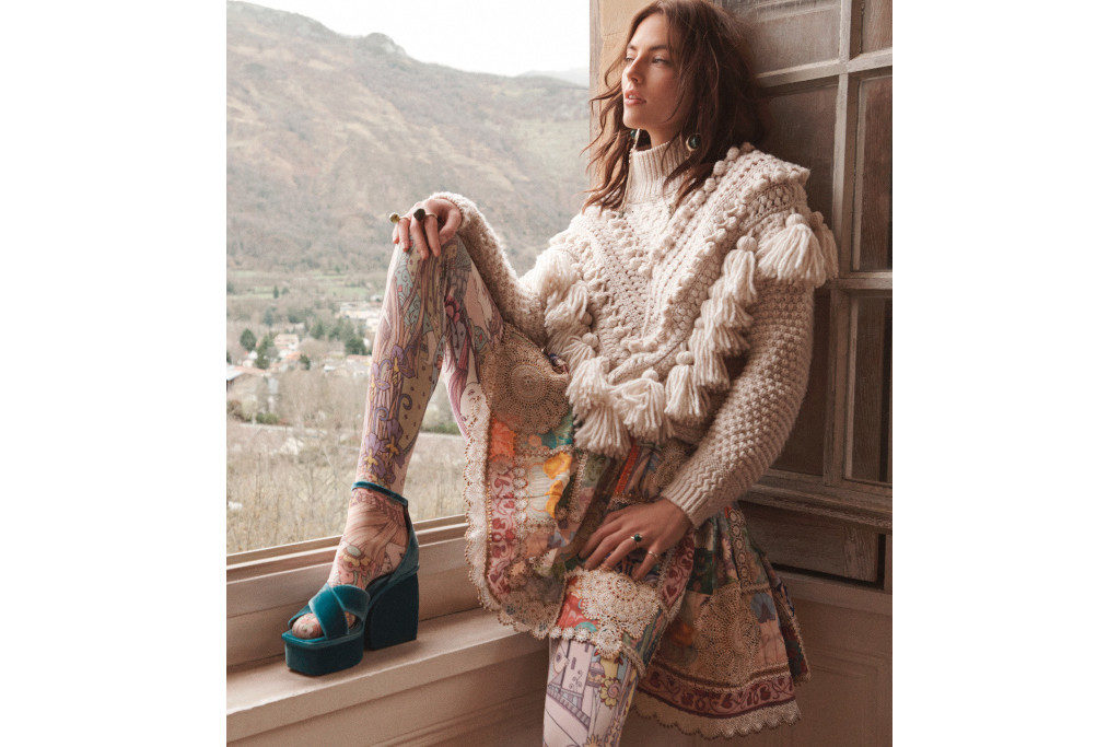 Model sat on windowsill wearing a chunky wool knit jumper and floral skirt, with leg propped up to reveal white lace tights and teal velvet platform heels