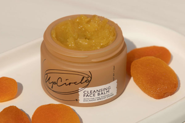 Tub of skin cream surrounding by apricots